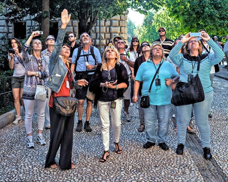 Granada, Spain - September 19, 2015: A female tour guide indicates a point of interest to a group of adult male and female visitors in Granada, Spain, some engaged in photographing.