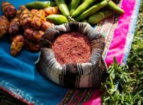 Andean tubers and green pods arranged around a bowl of colorful seeds